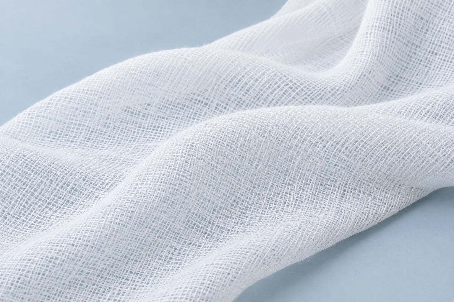 A continuous length of white cotton medical gauze in soft natural folds, showing its fine weave